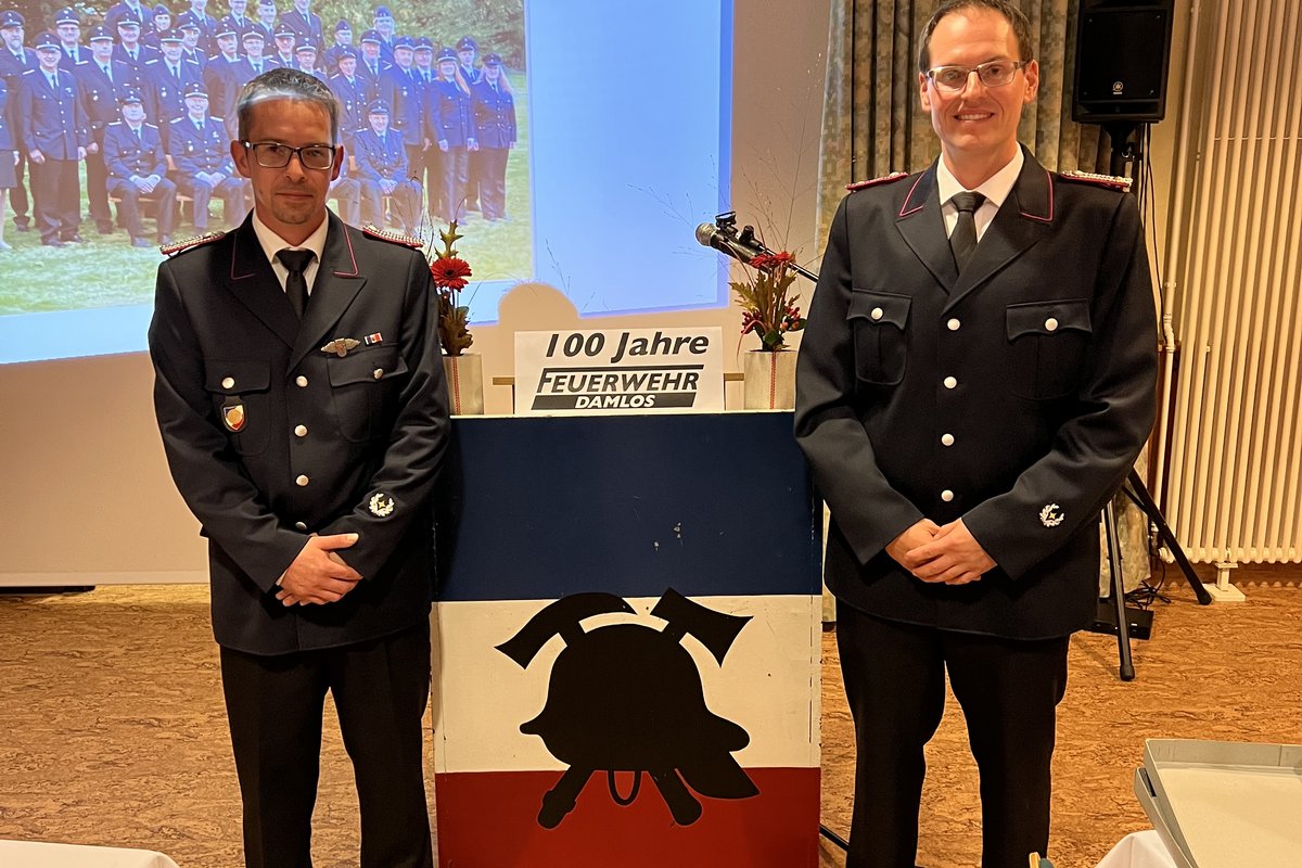 2 Feuerwehrmitglieder stehen vor einer Leinwand zur 100-Jahr-Feier